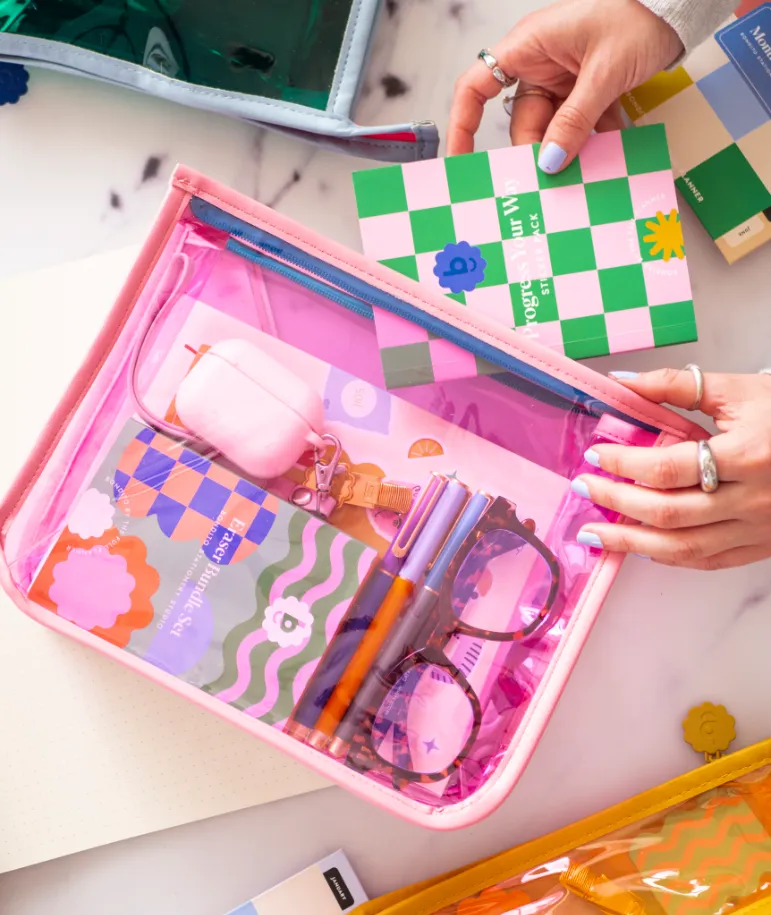 Estuche rosado transparente con accesorios de papelería, lentes y llavero