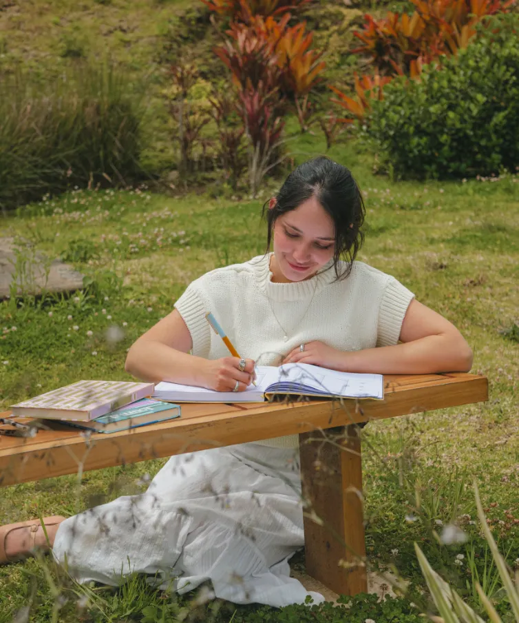 Mujer escribiendo en un planner de The Full Planner en un banco de madera en el jardín